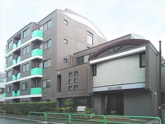 グレーの5階建ての建物は重厚感があり、緑の柵がついたベランダが付き、周辺には緑が植えられている。