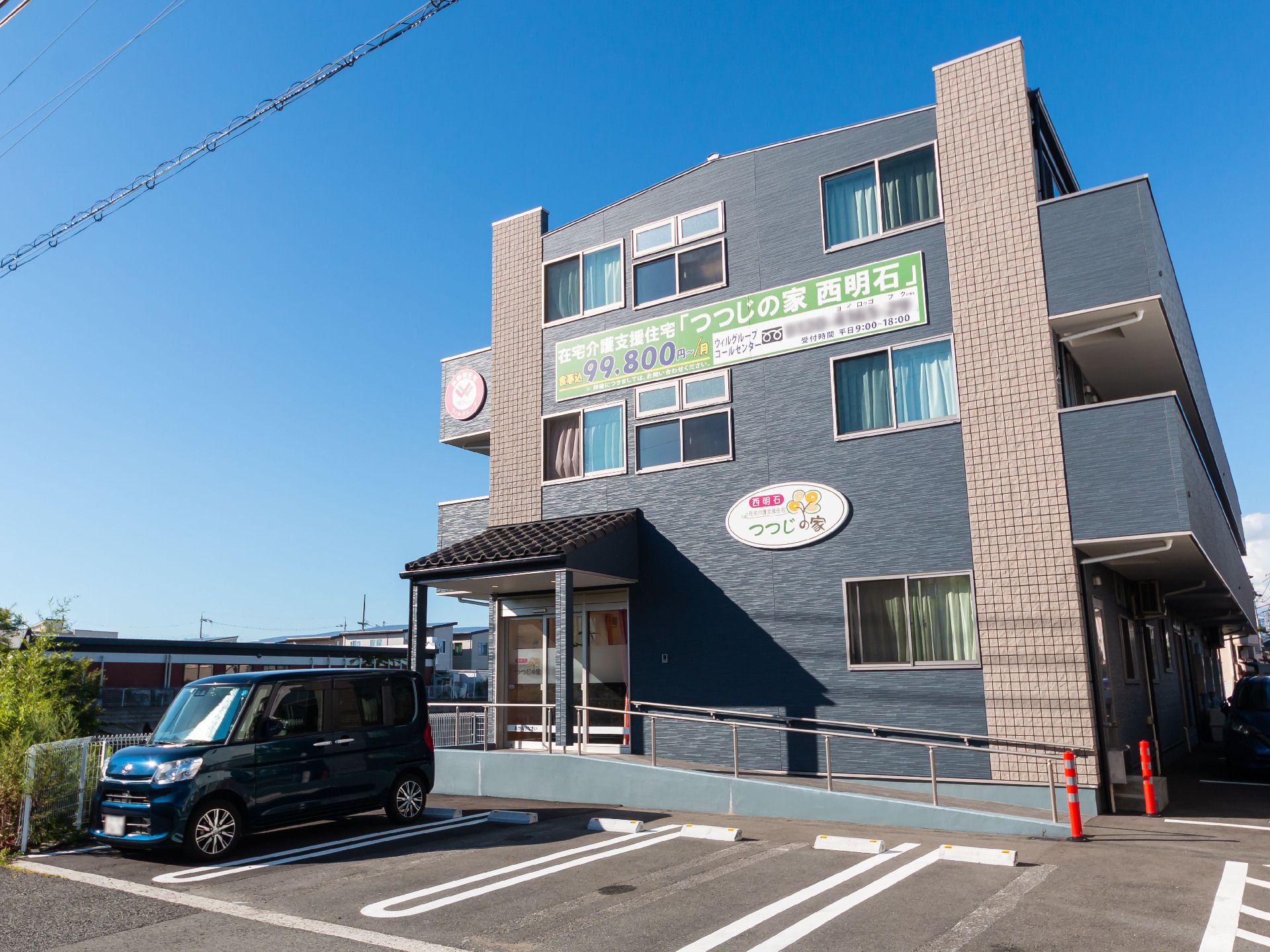 目の前に車が止まっている駐車場があるグレーの外観で３階建ての建物