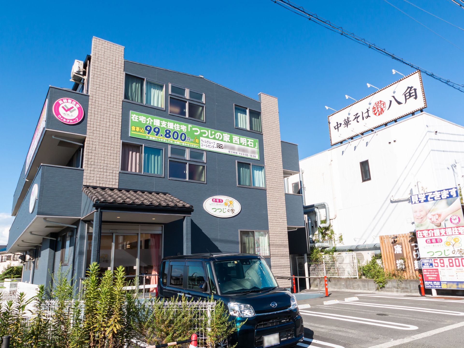 目の前に車が止まっている駐車場があるグレーの外観で３階建ての建物