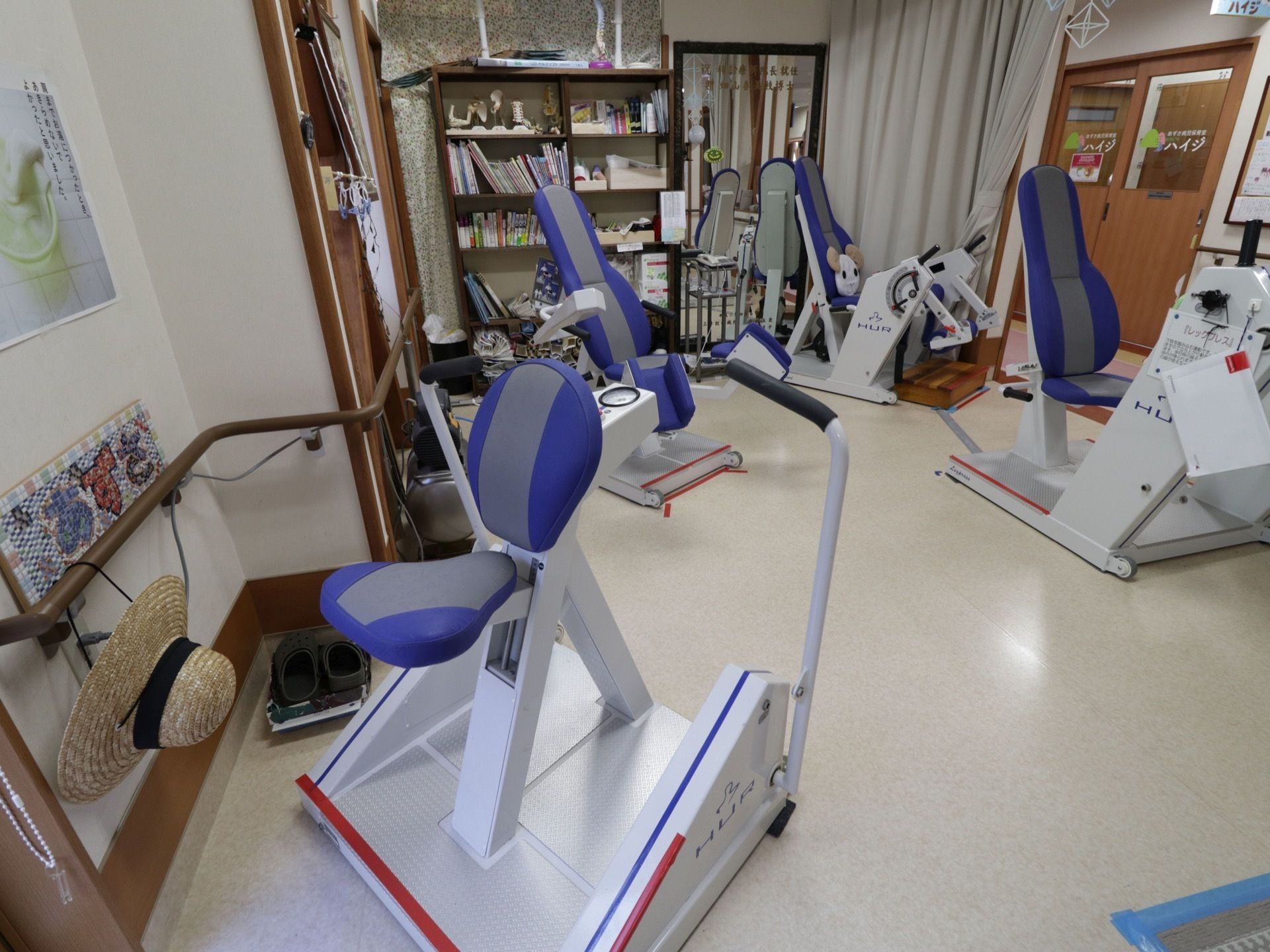 身体の衰えを改善するための機械が何種類も用意されている。棚には本や雑貨が置かれている。壁には鏡がついている。