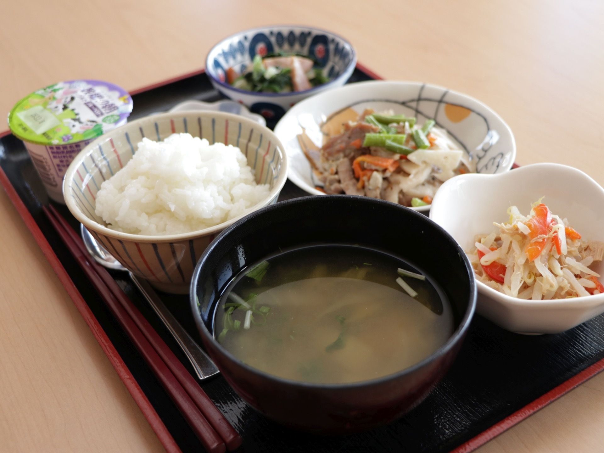 味噌汁と白米を基本とした和食である。野菜をたくさん使った主菜、副菜、小鉢が並んでいる。デザートにヨーグルトが用意されている。