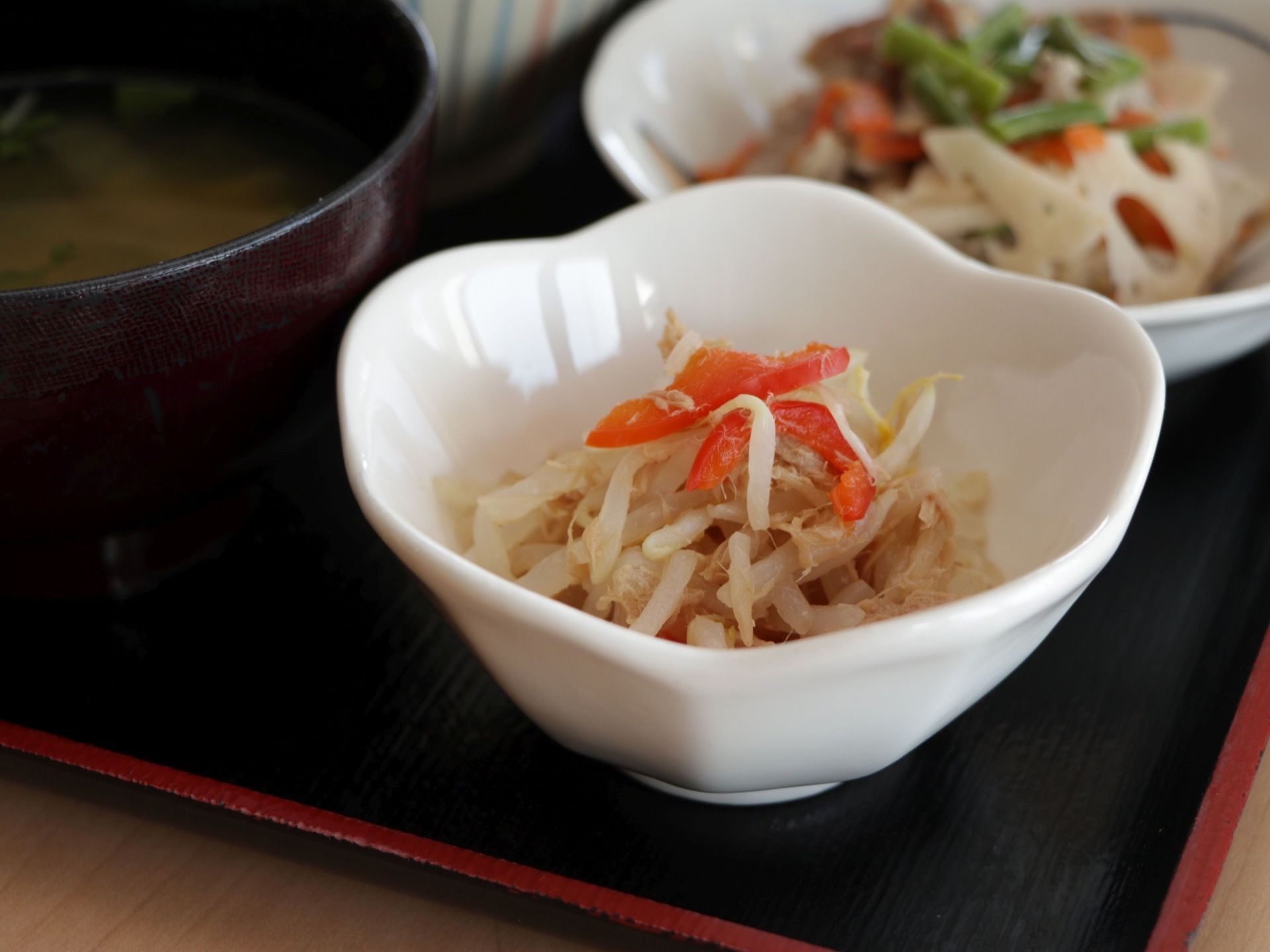 もやしと赤いパプリカをふんだんに使った副菜である。小さめの白い深皿に盛りつけられている。お盆の上に用意されている。