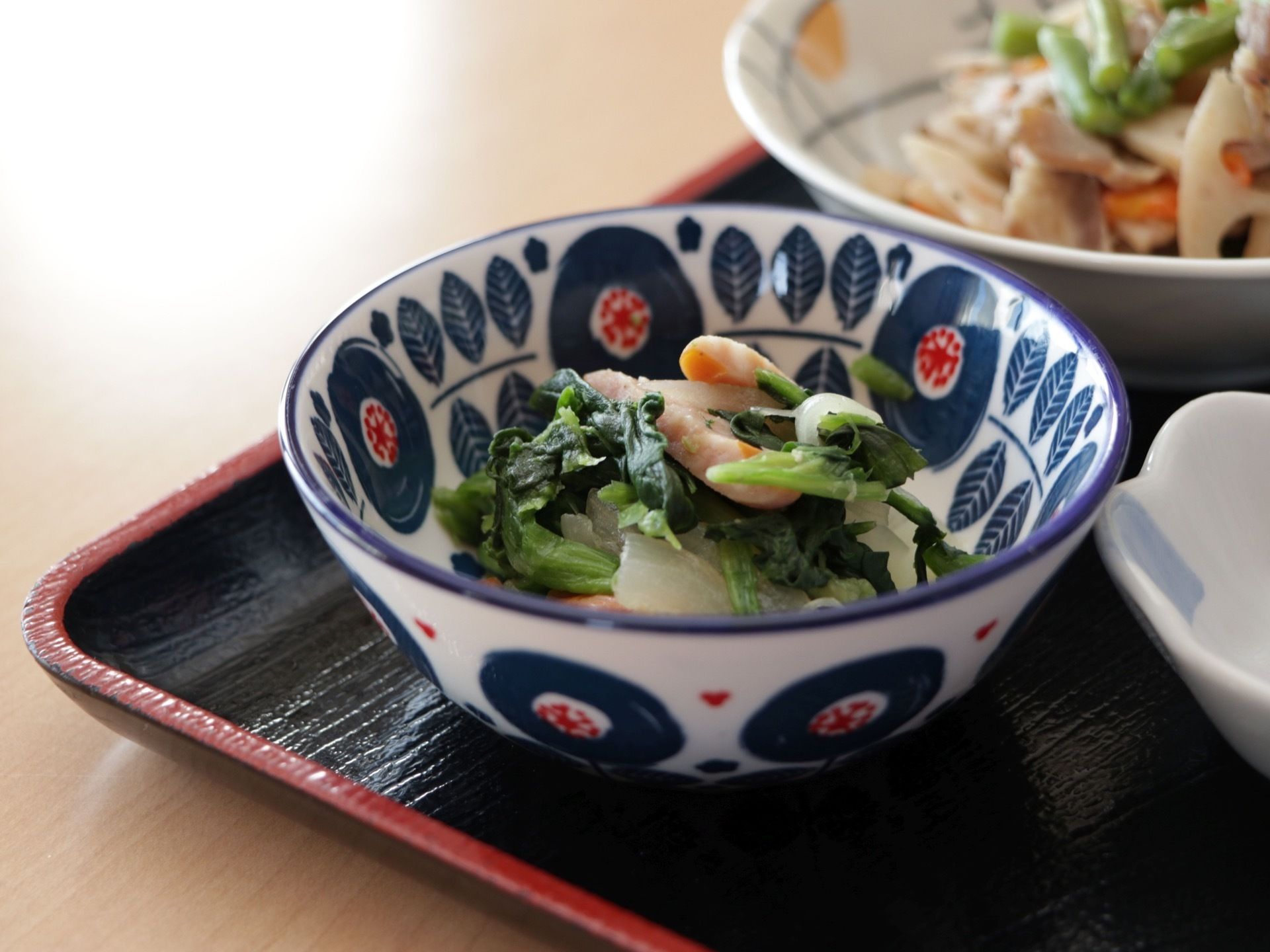 青菜と海老の和え物が小鉢に盛られている。その奥にはレンコンを使った根菜類のおかずが用意されている。彩り豊かである。