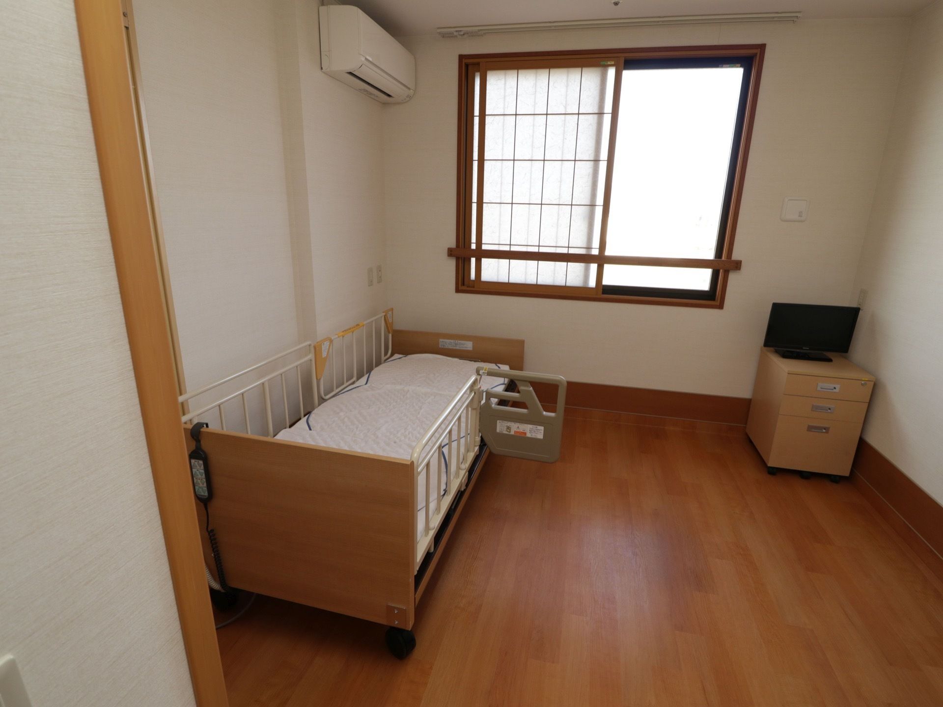 大きな窓は障子窓になっている。柵のついたベッドが用意されている。エアコンとテレビ、テレビ台が完備されている。