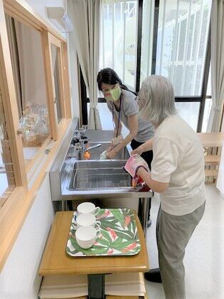 食器洗いを手伝う高齢者とスタッフの様子。何かを話している様子