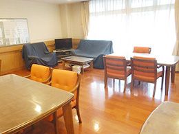 オレンジの椅子がセットされたダイニングテーブルが二組置かれ、奥には黒いレザー調のソファが置かれたリビングスペースがある。