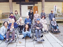 スタッフが付き添い外出を楽しんでいる高齢者たち。車いすを利用している人が多く、長袖の服を着ている。