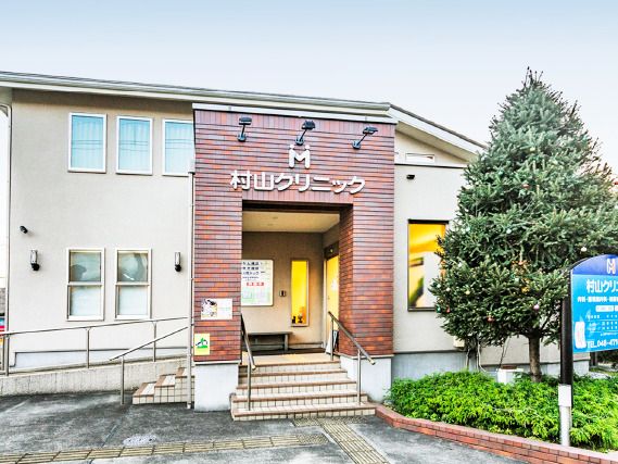 「村山クリニック」と書かれたレンガ調の外壁の建物は2階建てで周りには手すり付きの階段やスロープもある。