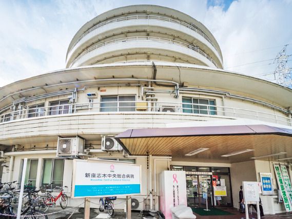 円形の建物は2階建てで、その後ろにも大きな建物があり、病院名が書かれた看板が建物の前にある。