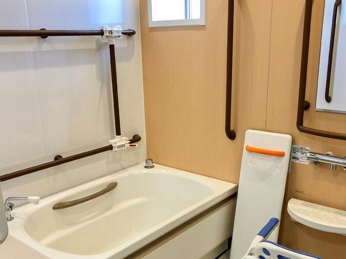 一人用の浴槽の周りにはたくさんの手すりが付き、シャワーの前にはシャワーチェアがあり、バスボードも壁に立てかけられている。