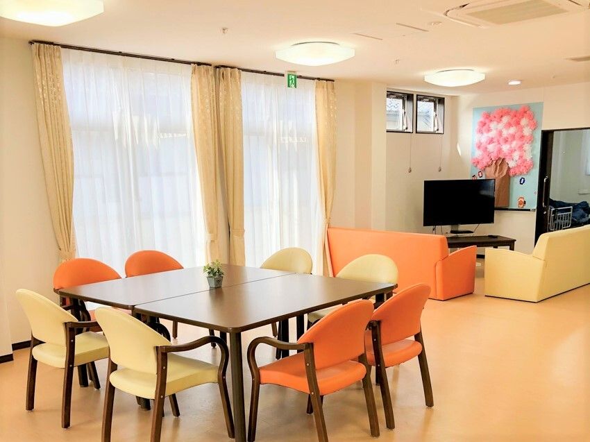 手前には小さな一輪挿しが置かれたダイニングテーブルがあり、奥にはテレビを囲んだソファスペースがあり、壁には桜の壁画が飾られている。