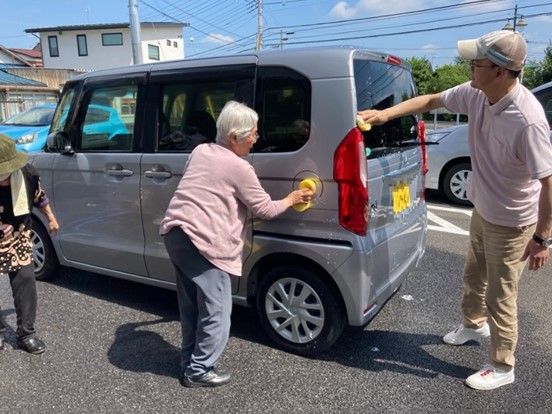 2階建ての建物は1階部分と2階部分の外壁の色が異なり、玄関部分には屋根が付き、ベンチも置かれている。広い駐車場にはのぼりも立っている。