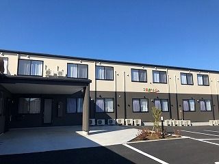 2階建ての建物は各フロアで外壁の色が異なり、玄関には大きな屋根があり、駐車場も付いている。
