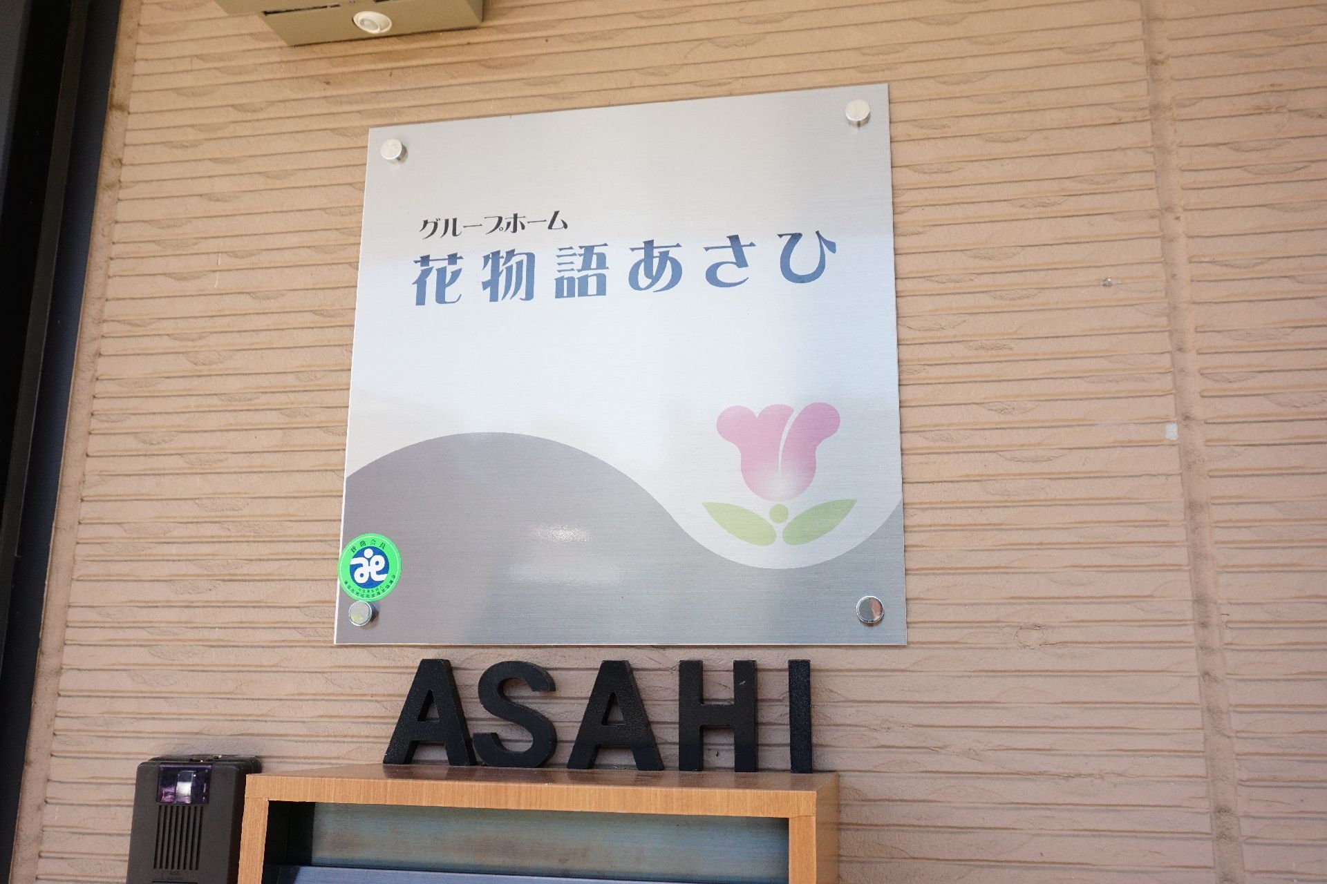 玄関付近に設置され、施設の名前とロゴが記されている看板