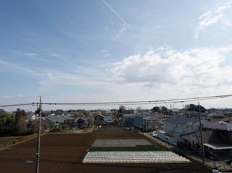 青い空の下に広がる街並み。住宅街の間には緑が点々とあり、畑も広がっているのどかな風景。