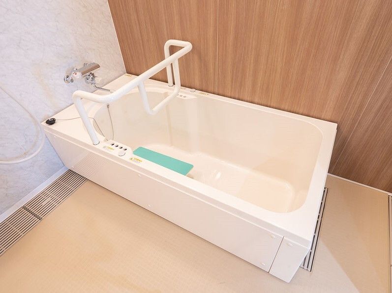 浴槽をまたぐ形で手すりが設置されていて、浴槽の深さもある。浴槽内には緑の小さなベンチのようなものがある。
