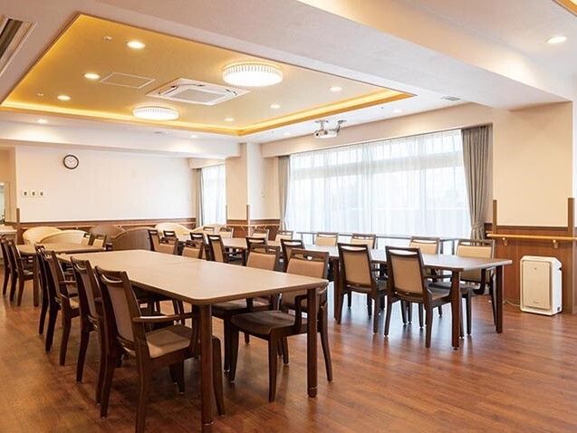 長細い大きなダイニングテーブルセットが複数置かれた食堂には大きな窓があり、カーテンも付いている。
