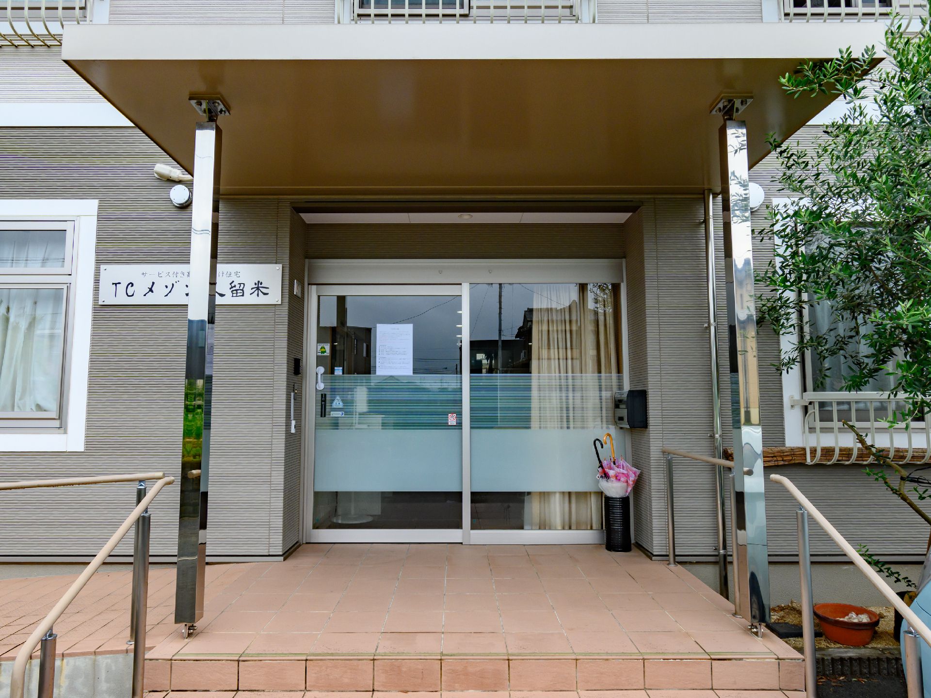 灰色の建物の屋根が付いた入り口前に設置された手すりに囲まれた階段