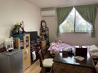 カーテンが付いた大きな窓がある部屋には寝具付きのベッドやテレビ、冷蔵庫、エアコンなどがあり、花も飾られている。