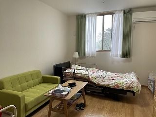 花柄の寝具付きのベッドやグリーンのソファ、ローテーブルが置かれたフローリングの部屋にはエアコンも付いている。