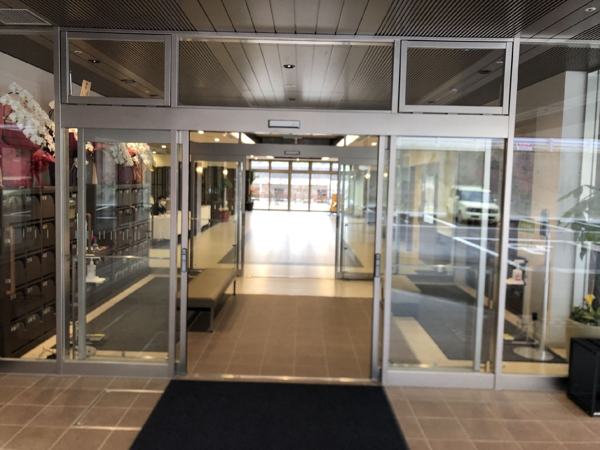 エントランスには段差がなく靴箱やベンチ、お祝いの蘭の花が咲いている。マットが敷かれ、観葉植物も置かれている。