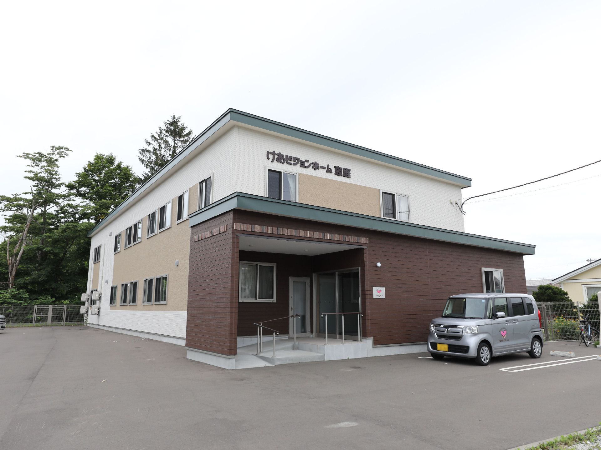 目の前にグレーの車が止まっている白い２階建ての建物