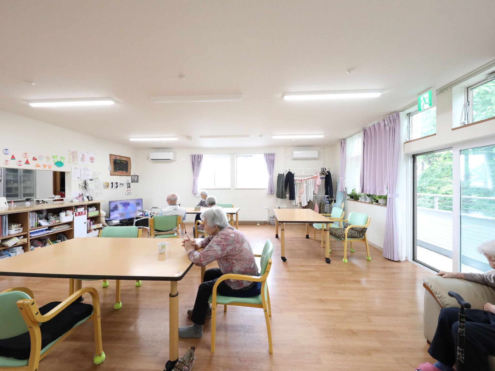 大きな窓に囲まれたダイニングに並んだ椅子に座っている入居者様