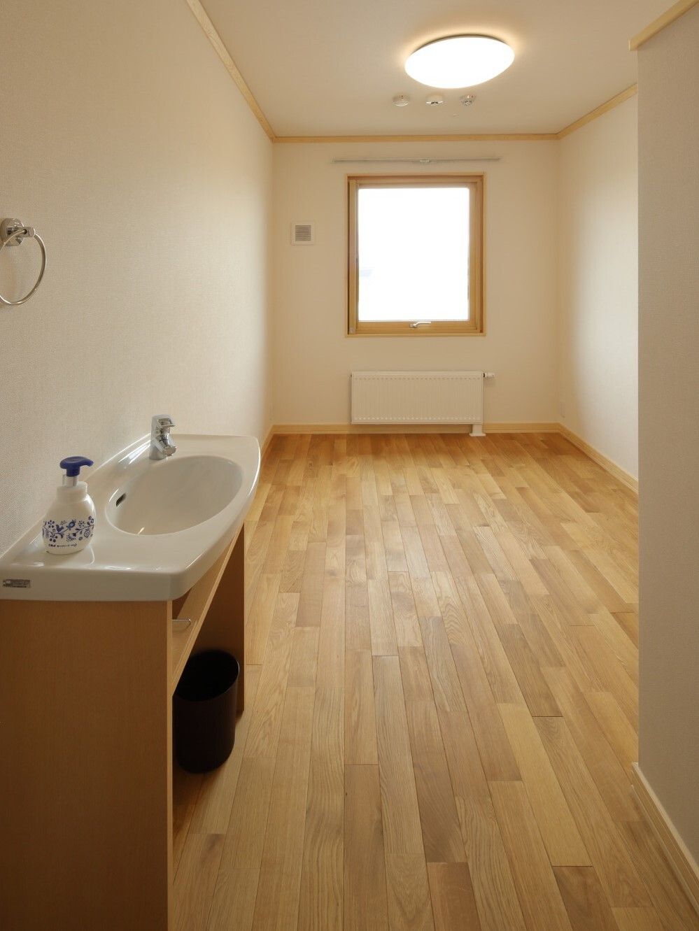 フローリング仕様の小さなワンルームタイプの部屋。手前に洗面台とトイレがある様子