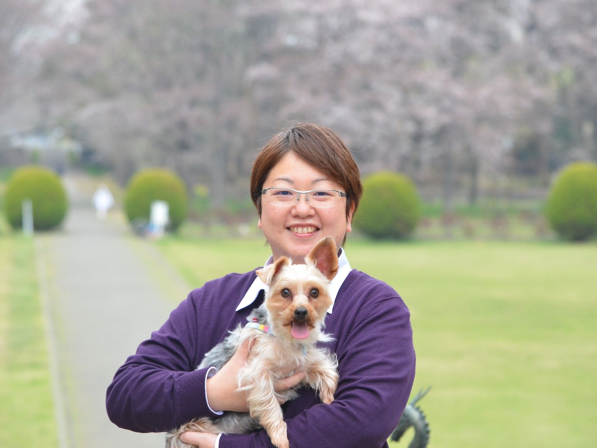 外に出て散歩している様子の車いすに乗る女性と施設スタッフの女性。笑顔で話している様子