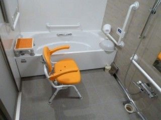 オレンジのシャワーチェアや浴槽内用ベンチが設置された一人用の浴槽が設置された浴室。