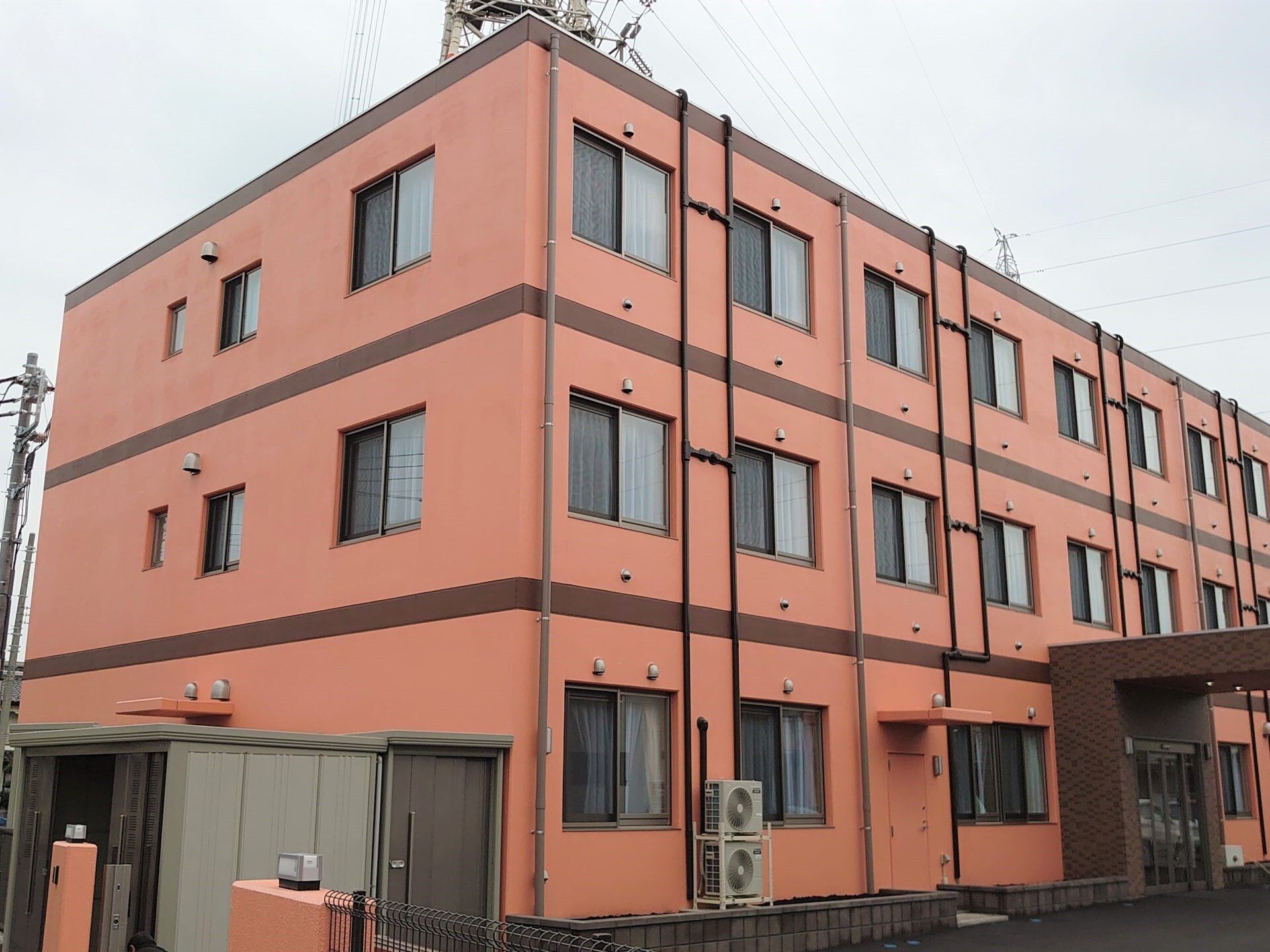 オレンジ系の外壁の3階建ての建物は横に長く、玄関には車寄せが付いている。
