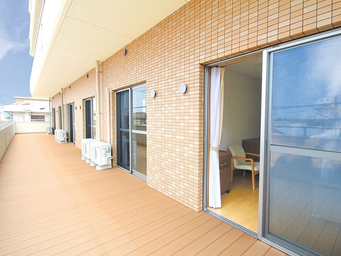 居室の窓が並んだバルコニー、バルコニーは広く、仕切りがなく、隣の部屋のバルコニーとつながっている。