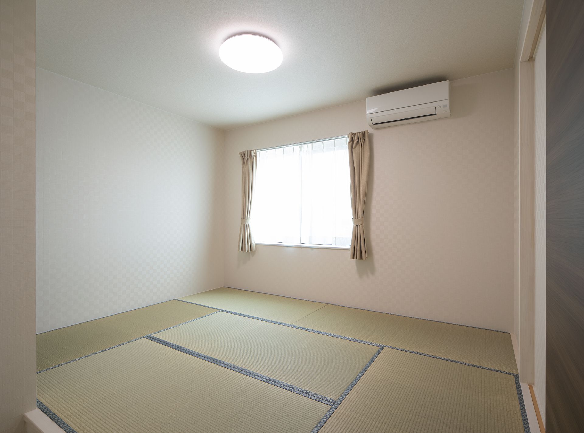 照明が天井に着き、大きな窓にはレースカーテンとカーテンが付いている畳敷きの和室。日当たりがよく、エアコンも設置されている。