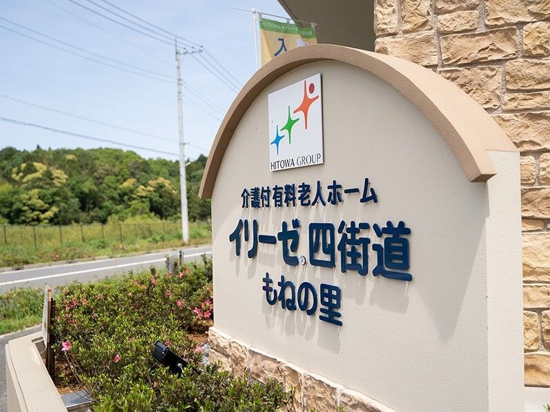 こちらを向いて笑顔になる車いすの高齢女性と介護施設の女性スタッフの様子