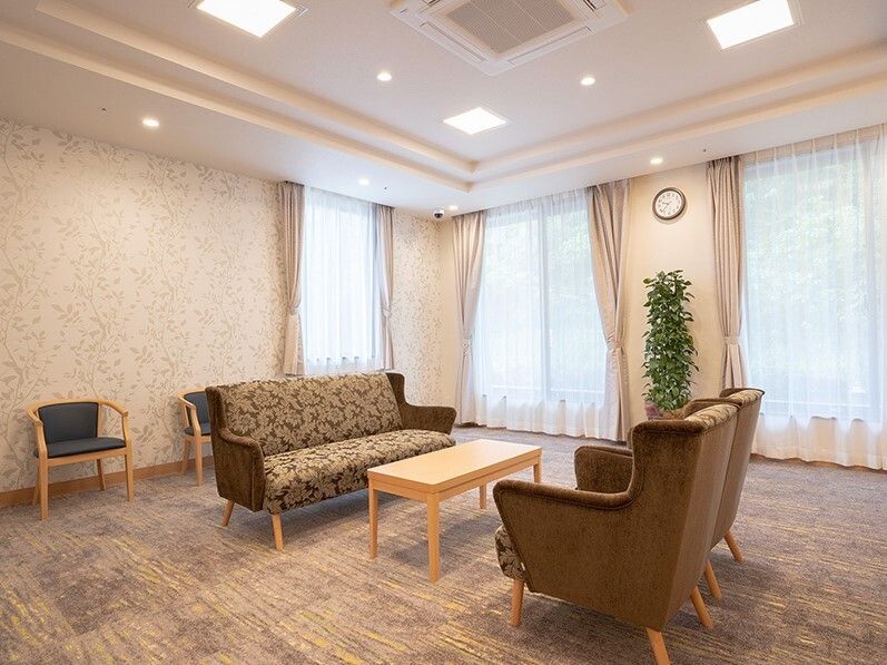 なにかを見て笑顔で手をたたいている高齢女性とスタッフの様子。施設での一場面の写真