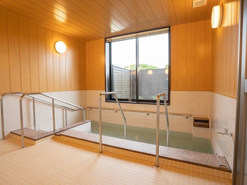 大きな浴槽の周りに手すりが付き、出入り口の階段にも手すりが付いた埋め込み式の浴槽が設置された浴室。