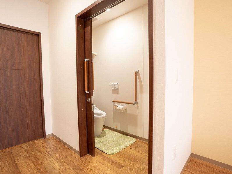 エル字型の手すりやオレンジの呼び出しボタンが付いたトイレは広く、スライド式のドアが付いている。