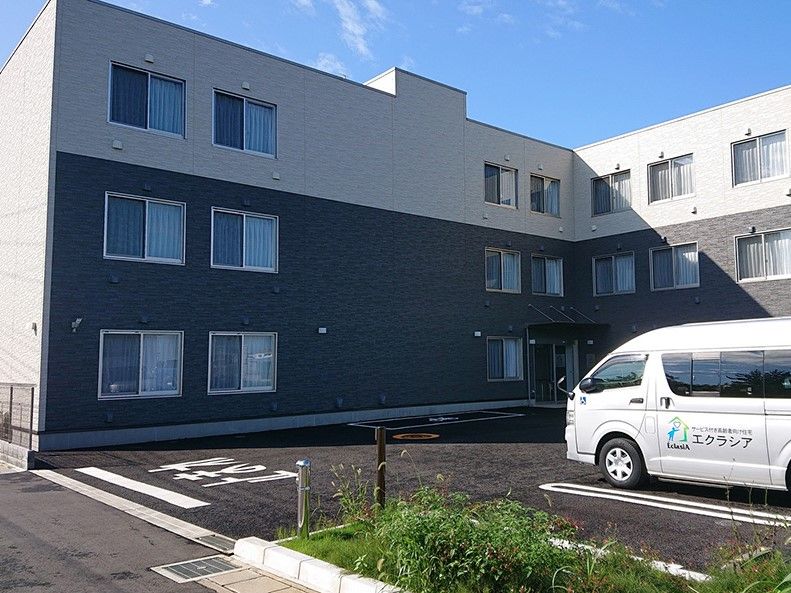 エクラシアと書かれているワゴン車が駐車スペースに停まっている、ツートンカラーの外壁の3階建て建築物