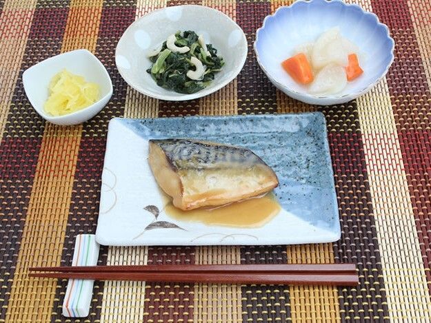 黒い円形の盆の上にかつ丼と豆腐とわかめの味噌汁、青菜の漬物が並べられている。漬物は細かく刻まれている。彩りがよくおいしそうな見た目。