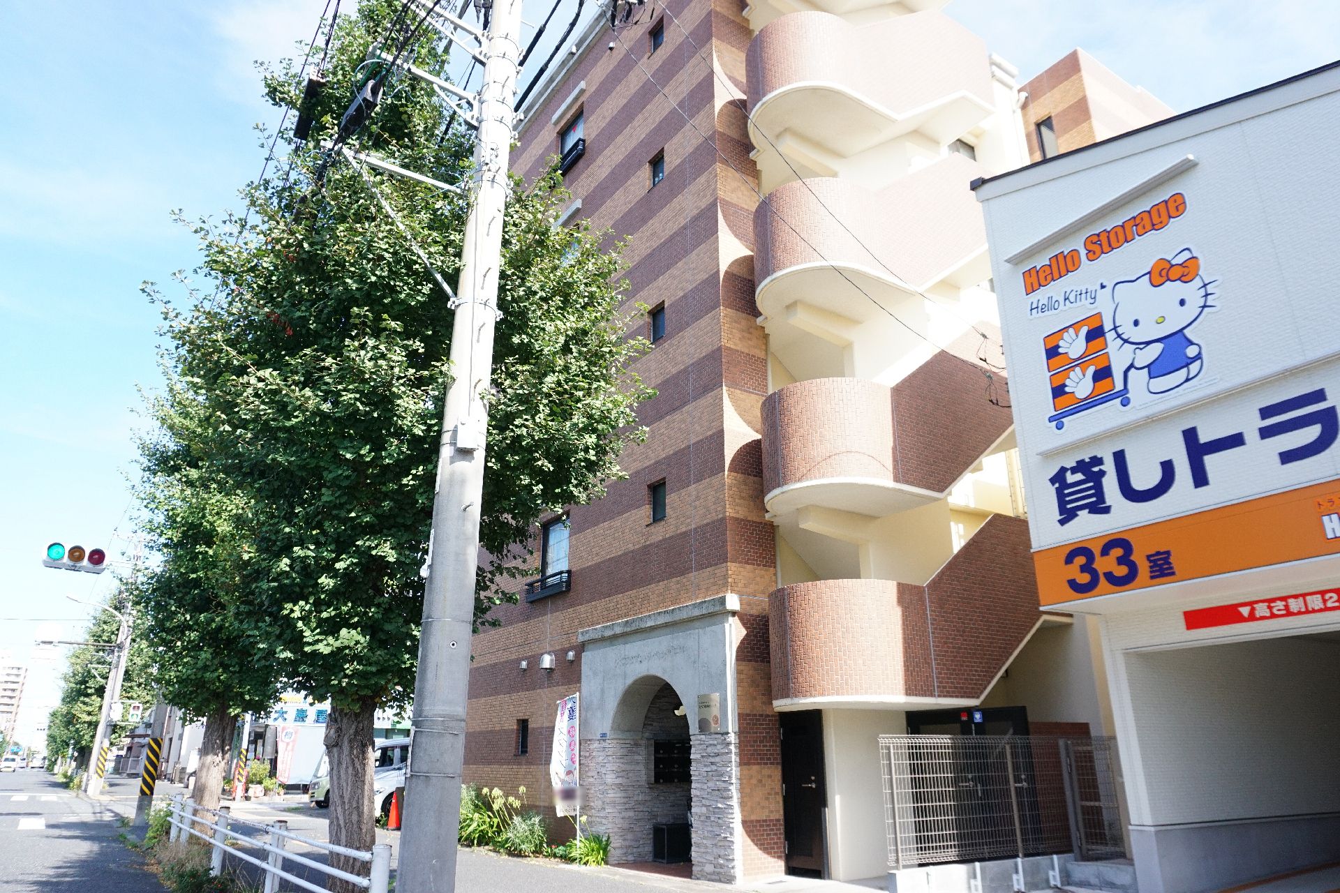 ブラウンとダークブラウンのストライプ柄の外壁が印象的な５階建ての建物。周辺には緑が多くあり、各フロアにベランダが付いている。