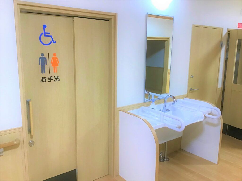 右側に車いすでも使える洗面台、左にトイレが写っている写真。施設内の共有スペース