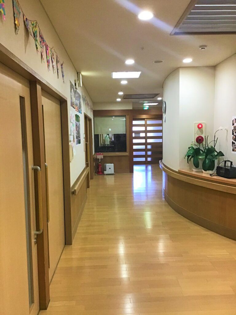 施設内の廊下の様子。手すりと個室のドア、飾り付けがある様子