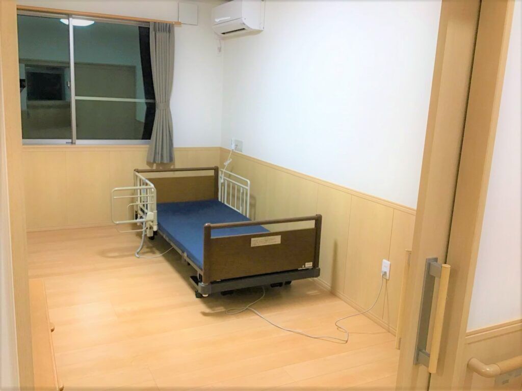 介護用ベッドとエアコン、窓がついている施設内の居室。グループホームの部屋