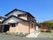 ベージュの外壁の2階建ての建物は一般の民家の様な外観。玄関先には屋根が付いていて、2階部分にはバルコニーがあり、庭先には洗濯物干し場もある。