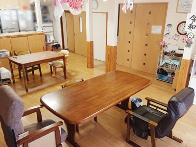 木製のダイニングテーブルが二組置かれたリビングダイニングには対面式のキッチンがあり、時計や似顔絵なども飾られている。