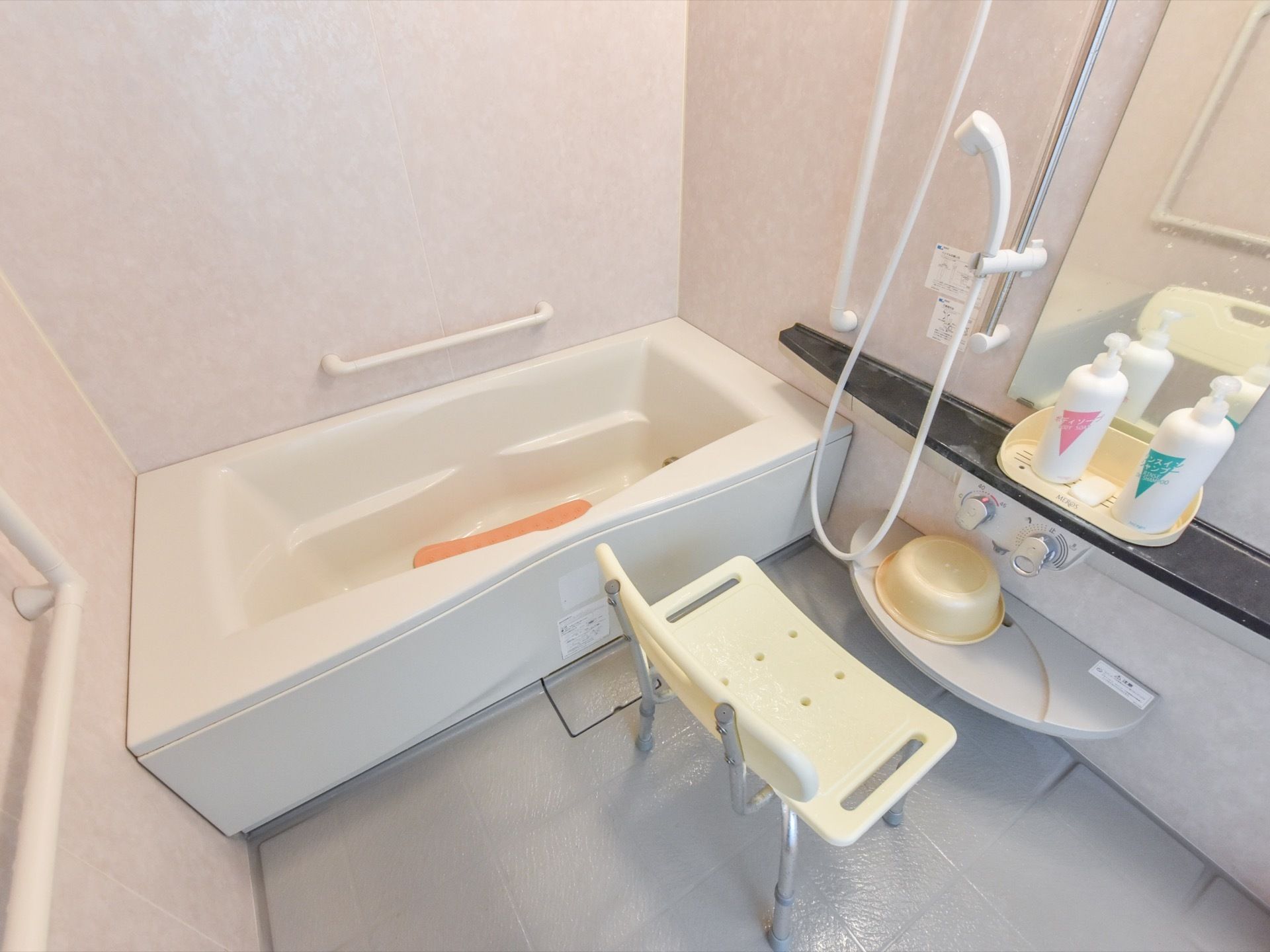 浴室の壁際には手すり付きの浴槽があり、シャワーエリアにはシャンプーなど一通りの道具が鏡の付近に置かれている。