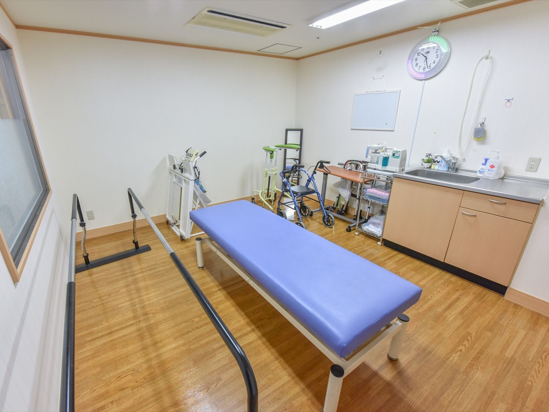 機能訓練室には各種リハビリ用装置のほか、洗面台があり、その上部にはアナログ式の時計も掛けられている。