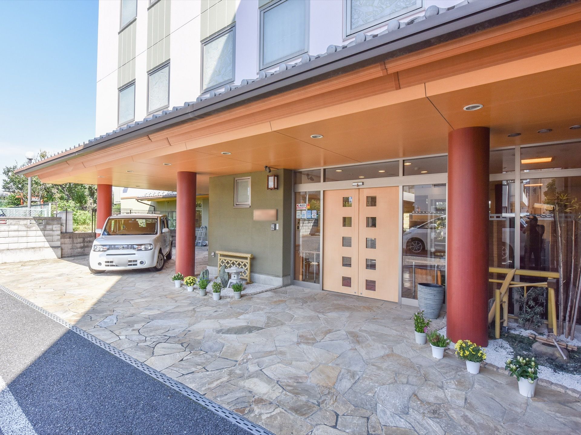 玄関部分には、３本の大きな赤色の柱に支えられる形で屋根が設置されており、その部分には大きな影ができている