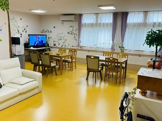 大きなテレビが設置された共有スペースには白いソファやテーブルセットが置かれ、観葉植物も飾られている。