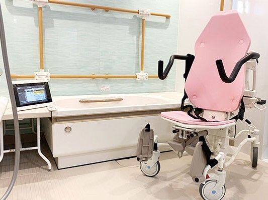 一人用の浴槽が設置された浴室にはピンクのリフトや、可動式の手すりもあり、浴槽の両サイドにはベンチもある。